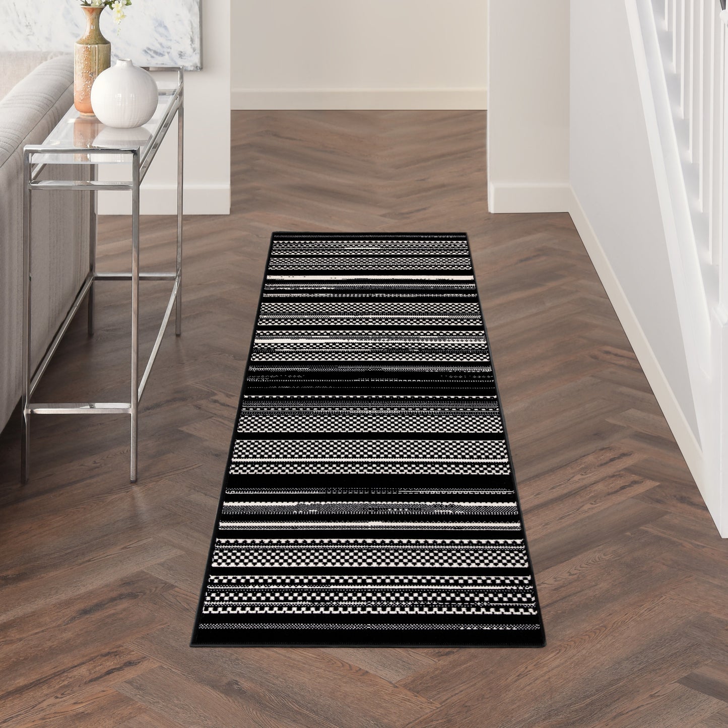 Long black-and-white striped hallway runner rug with geometric patterns on dark wood flooring.