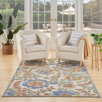 Two cream boucle armchairs with striped cushions flanking a multicolor floral area rug in a bright sunroom