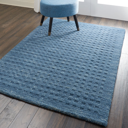 Blue rectangular textured rug with raised square pattern on dark wood floor, paired with a blue round ottoman.