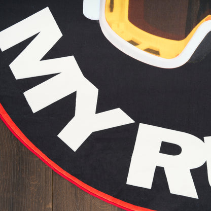 Round black rug with bold white letters and a yellow-orange ski goggles graphic, red border trim