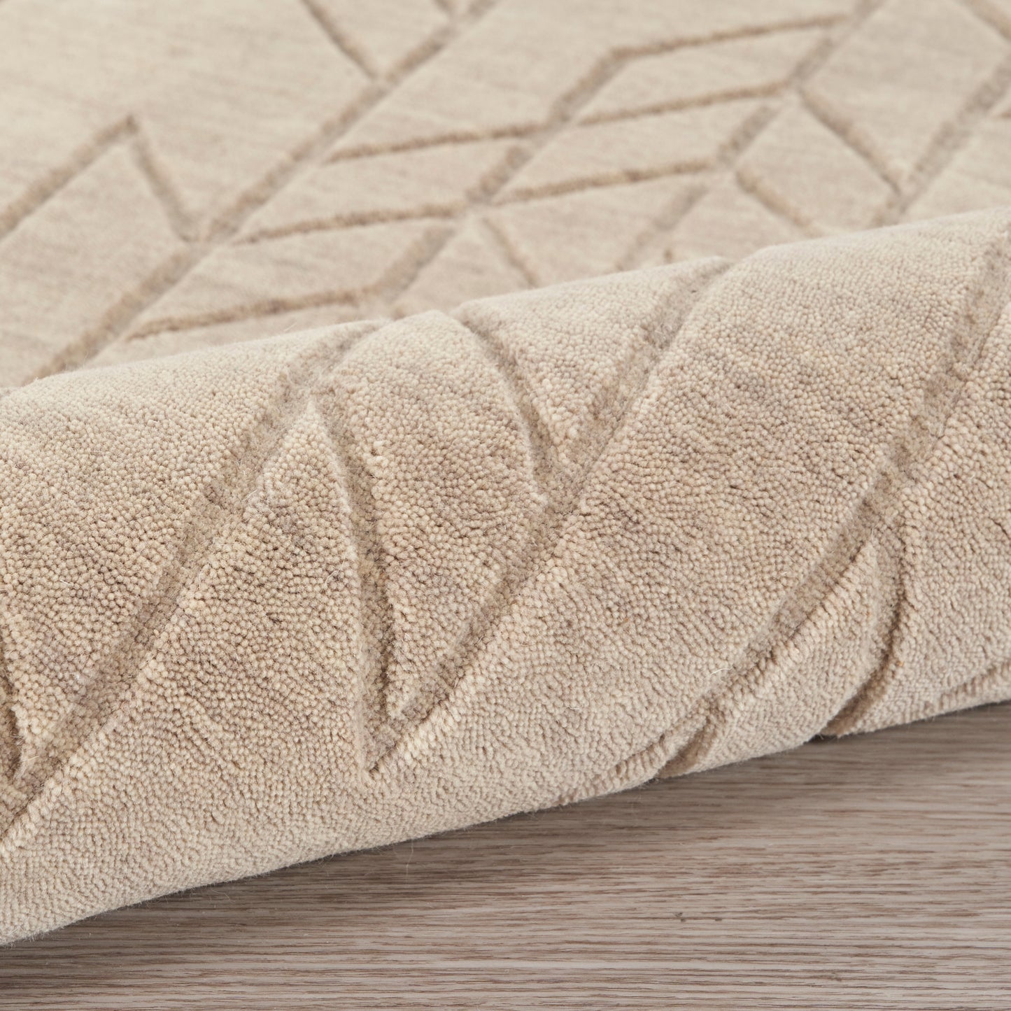 Beige plush rug with raised geometric diamonds pattern on light wood floor.