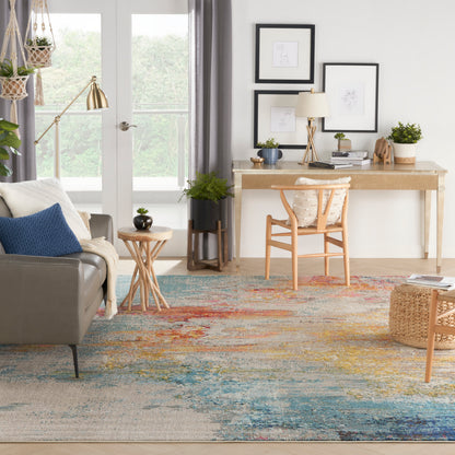 Bright living room with gray sofa, blue cushions, wooden desk and chair, colorful abstract rug, plants, and framed art