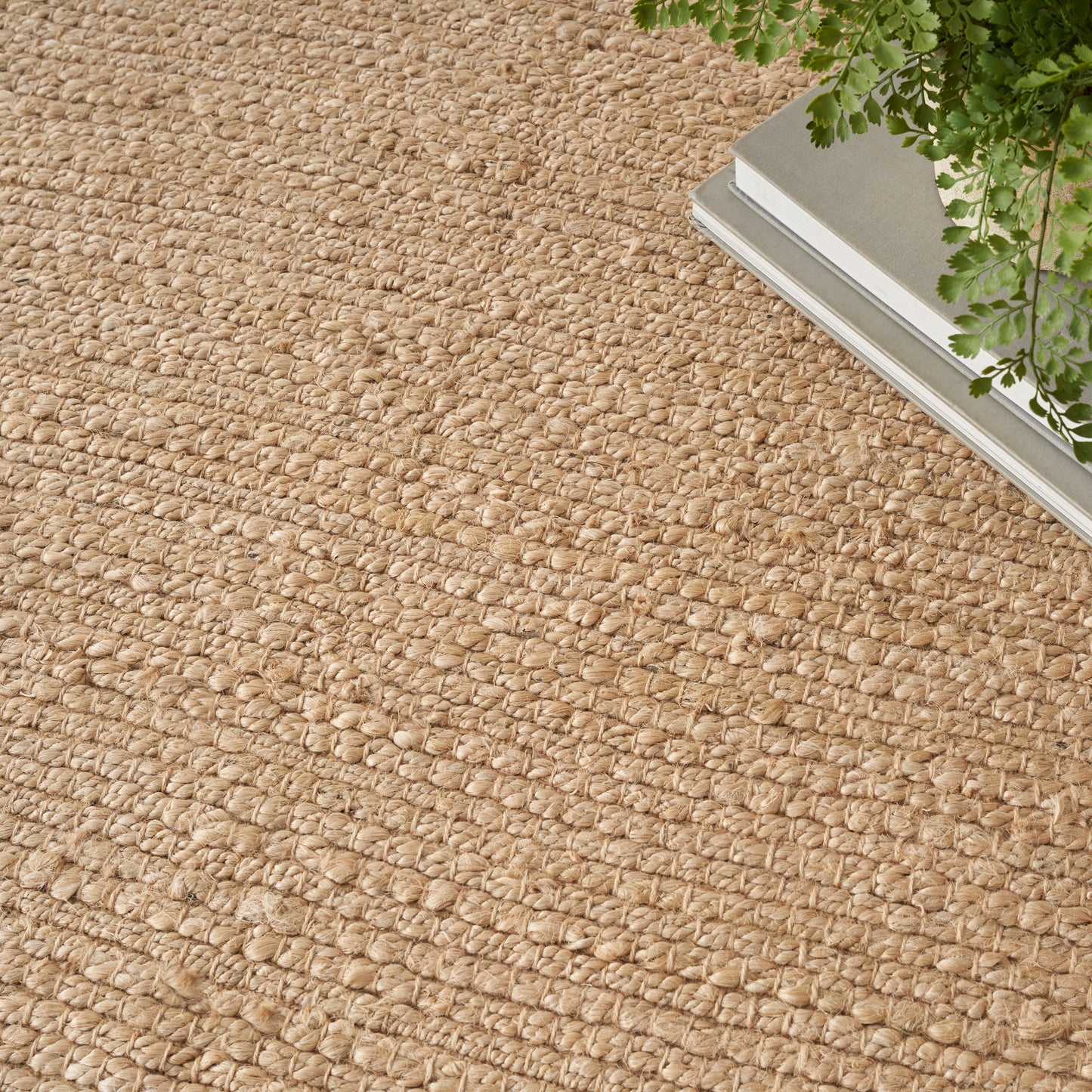 Natural beige jute rug with chunky loop weave; rectangular rustic boho style with greenery in a metal planter.