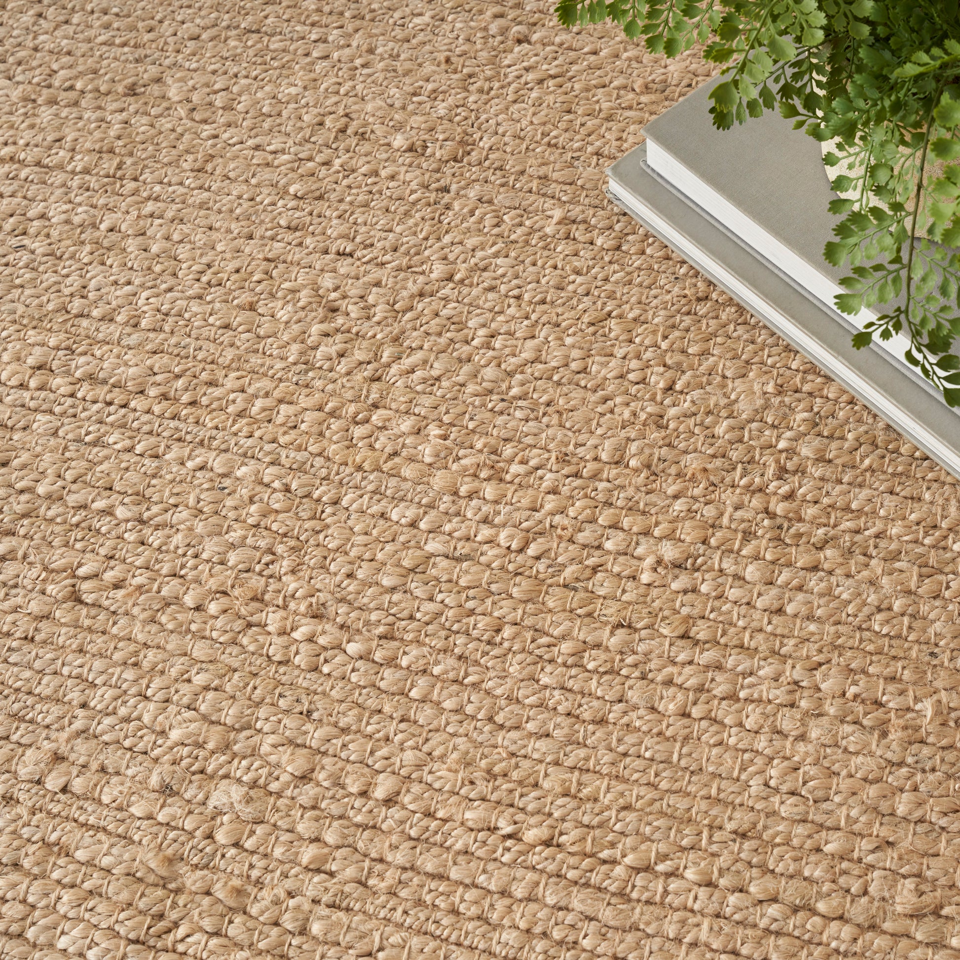 Natural beige jute rug with chunky loop weave; rectangular rustic boho style with greenery in a metal planter.