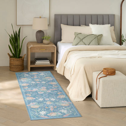 Blue floral runner on light wood floor beside a beige bed with a gray upholstered headboard, cream bedding, and a wooden nightstand.