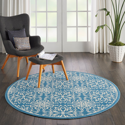 Round blue floral rug under a dark gray mid-century lounge chair and matching ottoman with wooden legs.