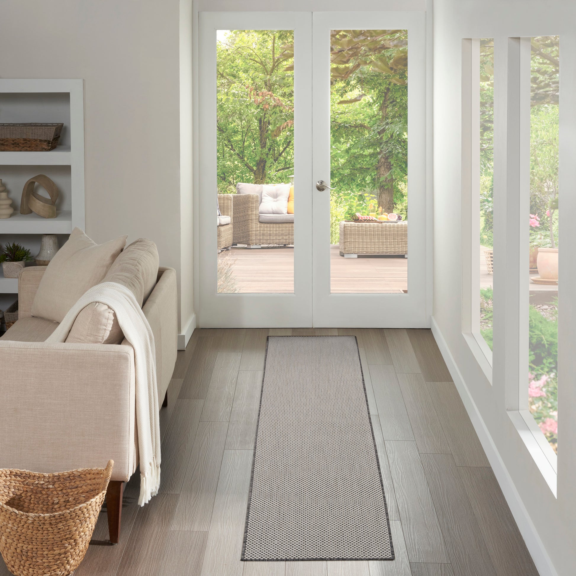 Grey woven runner rug in a hallway with a beige sofa and white walls, leading to glass doors and wicker seating.
