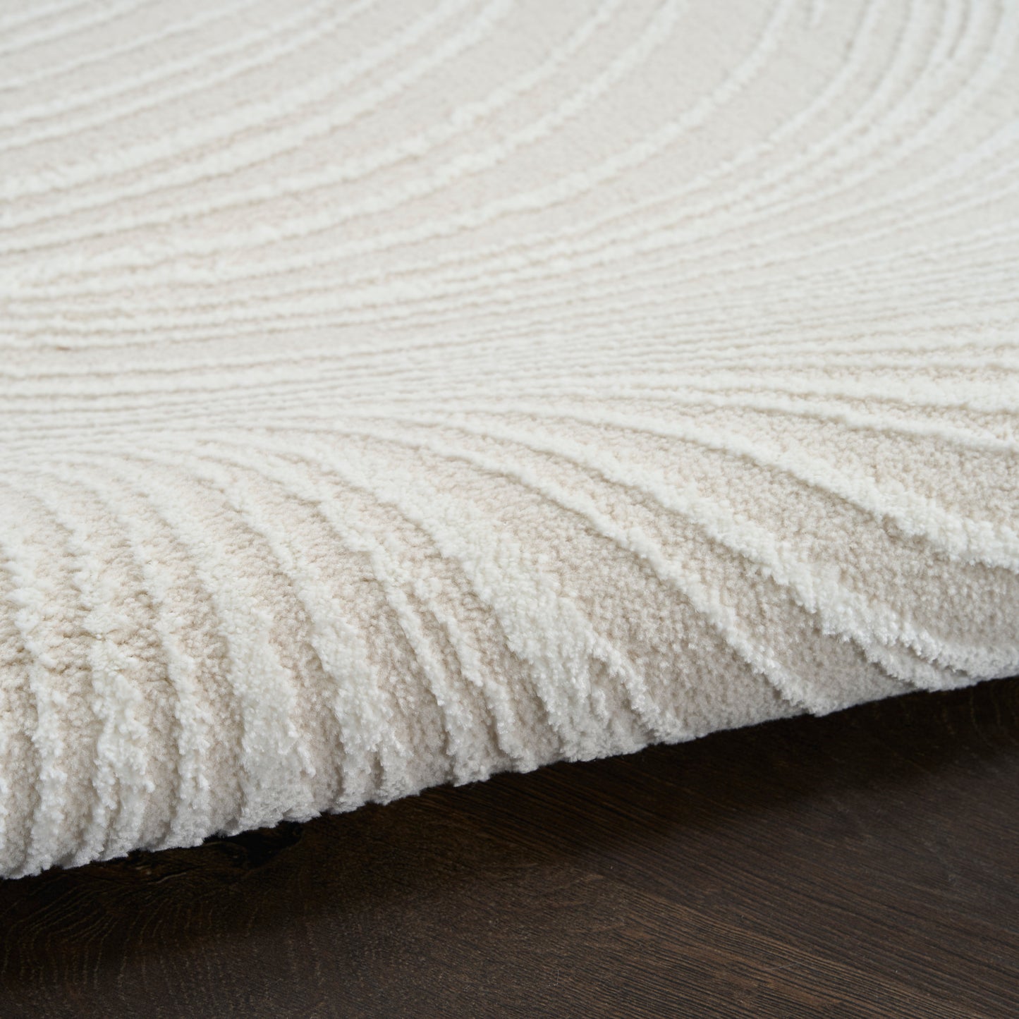 Cream plush rug with ribbed wave texture on dark wood floor.