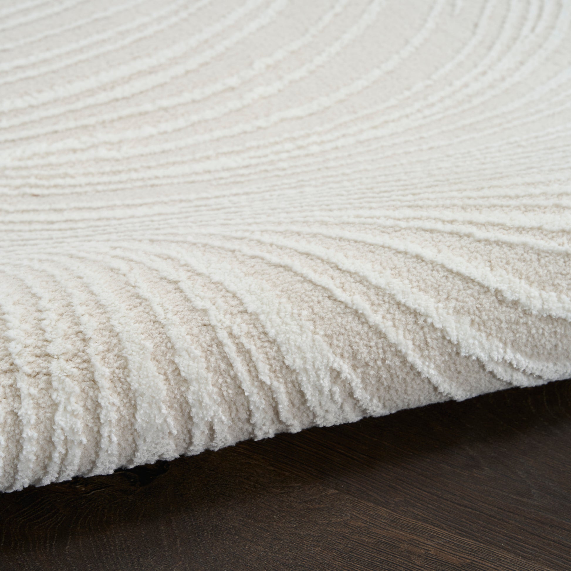 Cream plush rug with ribbed wave texture on dark wood floor.