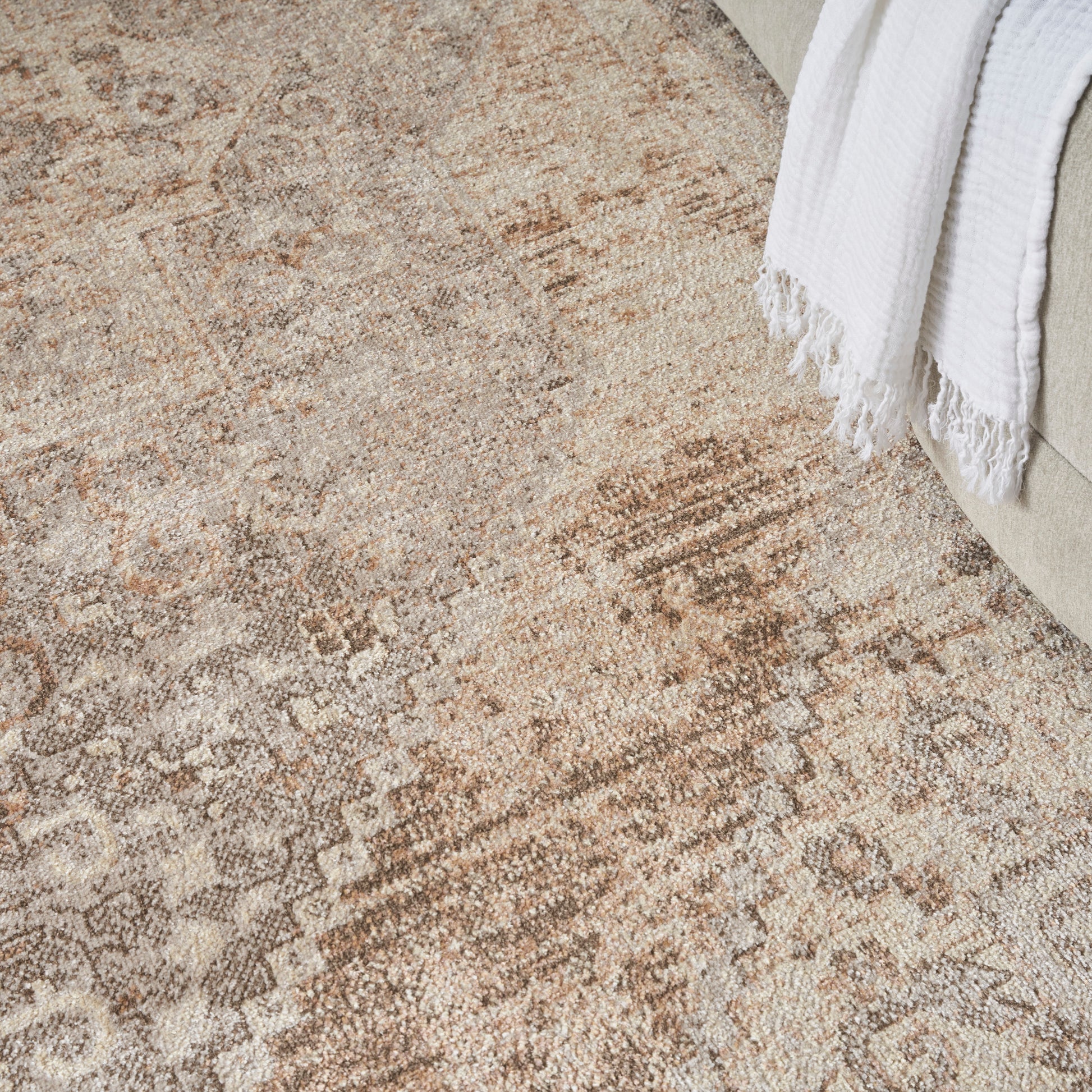 Distressed beige Persian-style area rug with tan and cream motifs beside a beige sofa and white throw blanket.