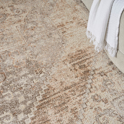 Distressed beige Persian-style area rug with tan and cream motifs beside a beige sofa and white throw blanket.