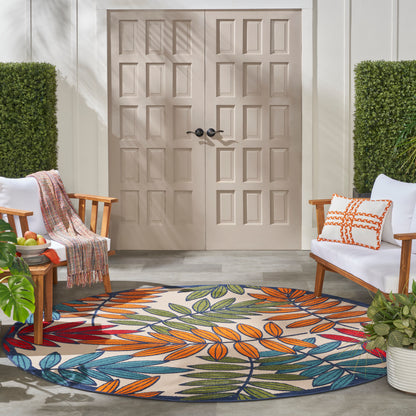 Round outdoor rug with multicolor leaf pattern on beige; wooden chairs, throw blanket, and plants on a porch.