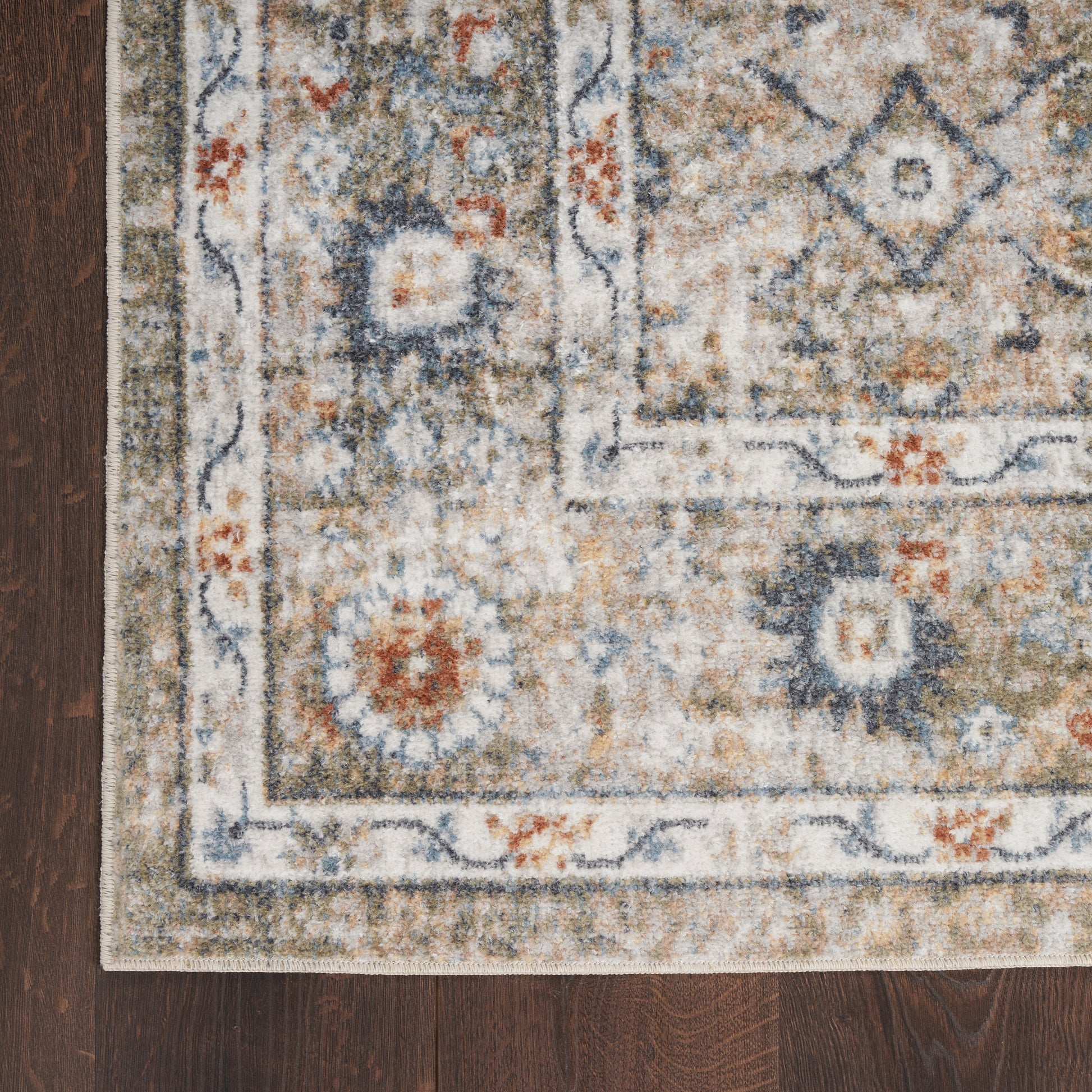 Rectangular oriental rug with beige, blue & rust motifs, floral border on dark wood floor.
