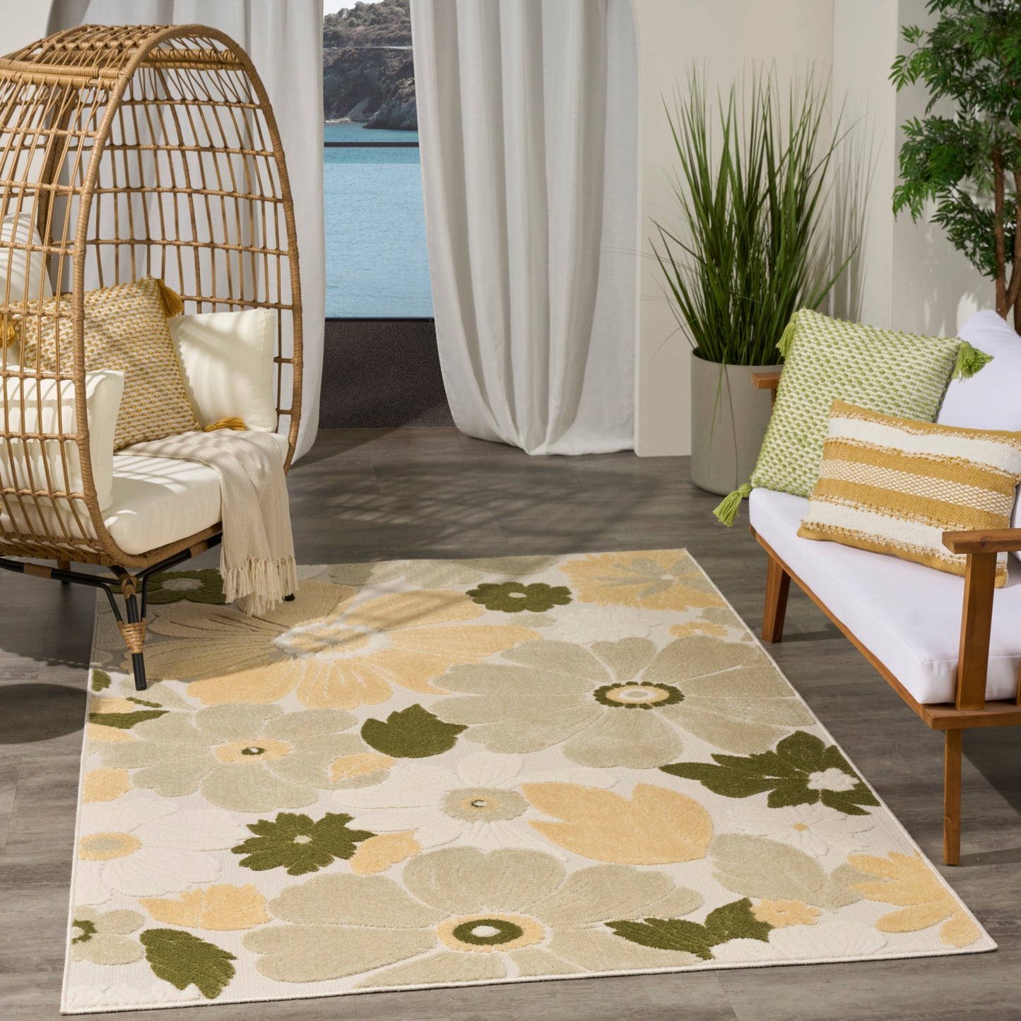 Floral beige, olive and pale-yellow area rug in a sunny living area with a wicker egg chair, wooden sofa, and tall plants.