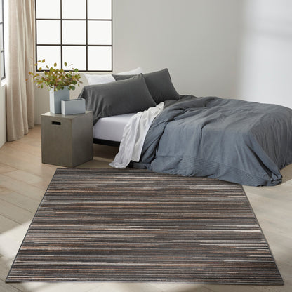 Modern bedroom with gray bedding, white throw, dark striped rug, concrete nightstand, and leafy plant near a grid window.