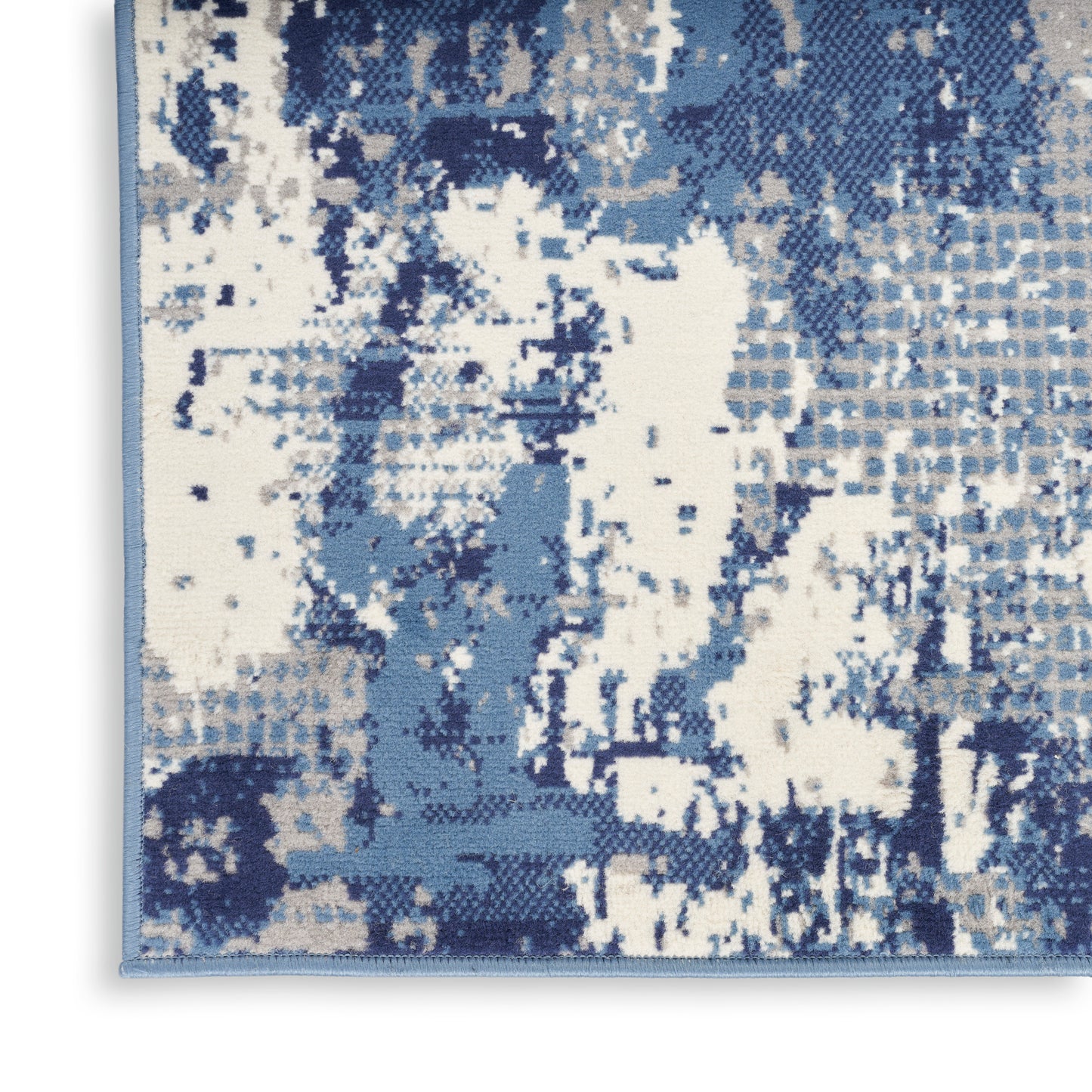 Rectangular abstract area rug in blue tones with white patches; pixelated woven pattern and light blue border.