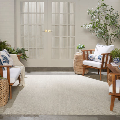 Bright sunroom with white French doors, cream rug, wooden lounge chairs with white cushions and blue pillows, surrounded by plants.