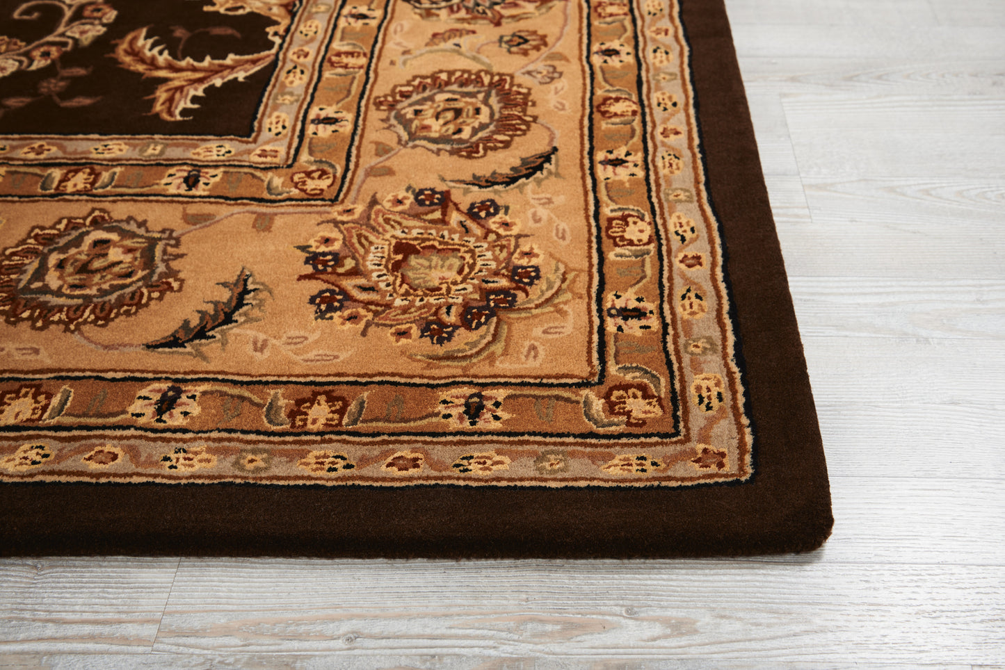 Persian-style area rug with dark brown border, tan accents and beige field with ornate floral motifs on light wood floor