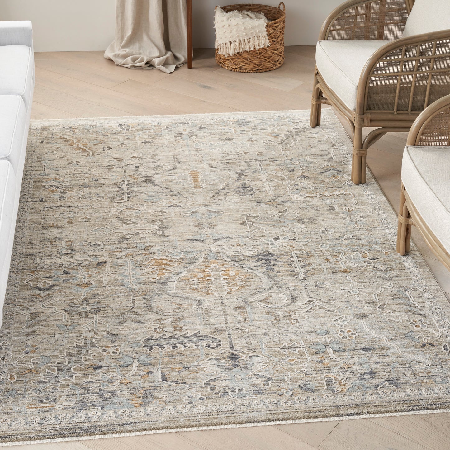 Neutral patterned area rug in beige, gray & blue tones on a light wood floor beside rattan seating.
