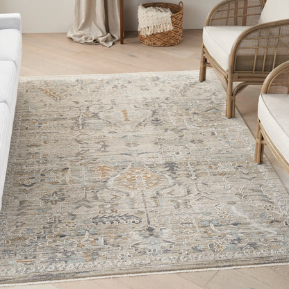 Neutral patterned area rug in beige, gray & blue tones on a light wood floor beside rattan seating.