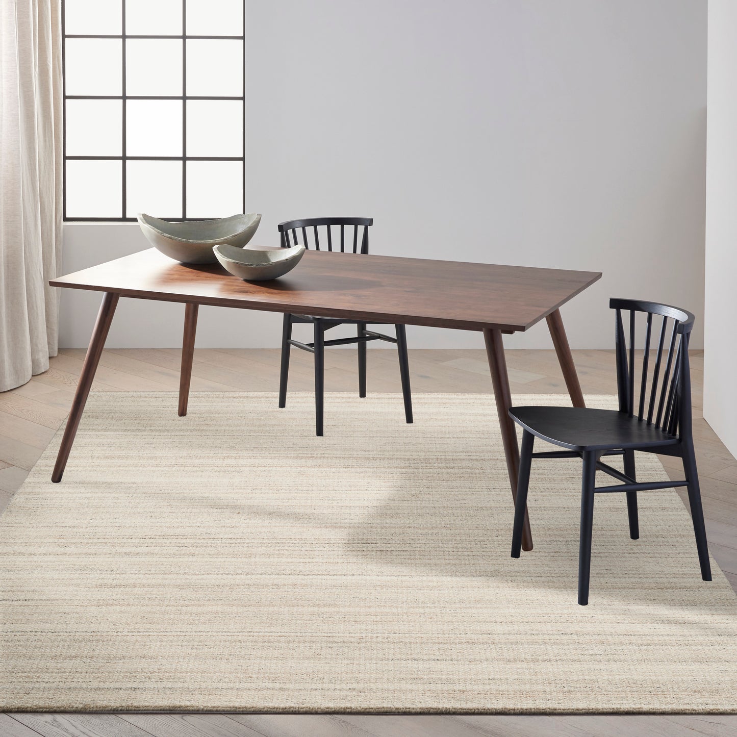 Dark walnut mid-century dining table with tapered legs, black Windsor chairs, ceramic bowls, sunlit beige rug.
