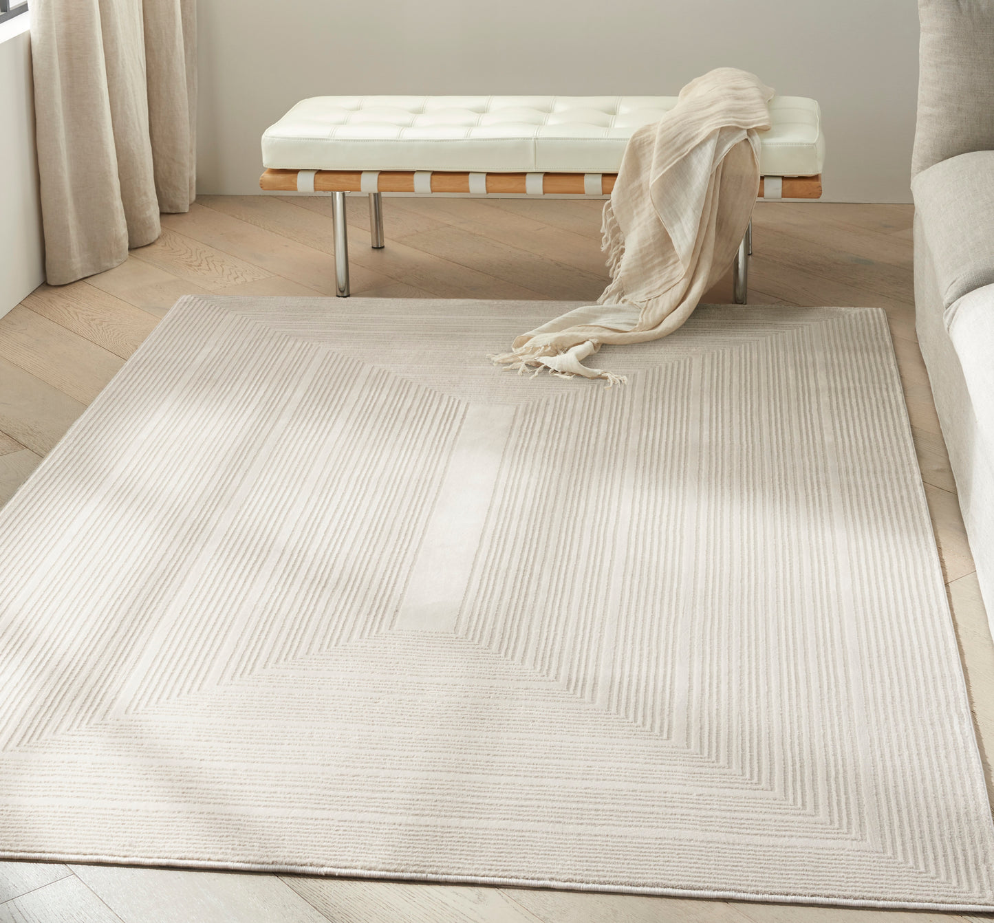 Cream geometric area rug with chevron lines in a bright living room, beside a white tufted bench with a beige throw.