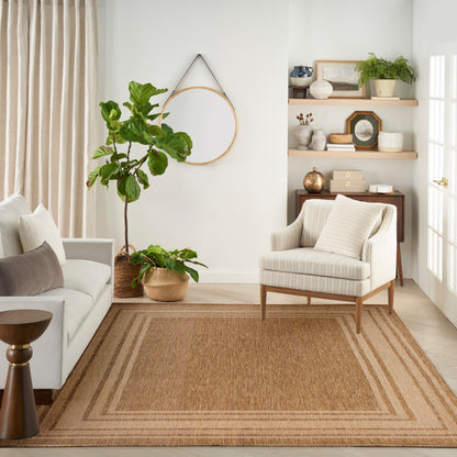 Bright beige living room with a beige sofa, striped armchair, and a large woven jute rug 10' x 14', potted plants, and wooden wall shelves.