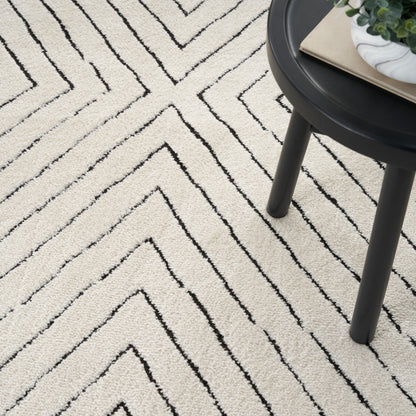 Beige plush rug with black chevron lines under a round black side table with a potted plant and books.