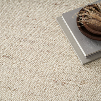 Beige boucle rug with stacked grey magazines and a brown wooden bowl holding dried grasses.