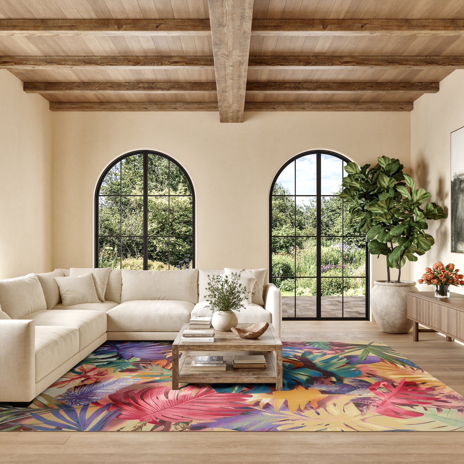 Neutral beige living room with a sectional sofa, colorful tropical rug, arched black-framed windows, wooden beam ceiling, and a potted plant.