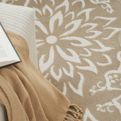 Beige rug with large white floral motif, paired with a draped tan knit blanket and an open book nearby.