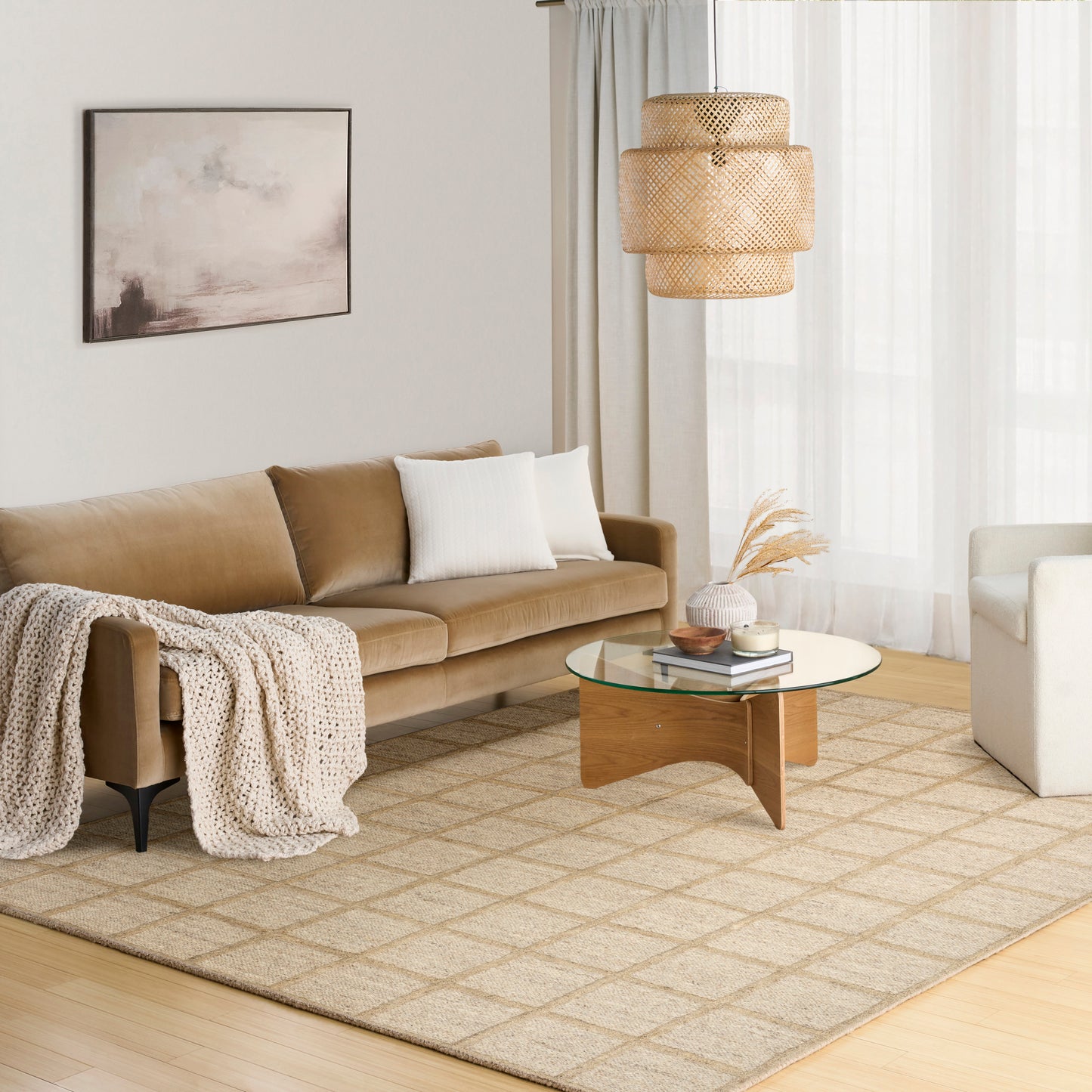 Cozy beige living room with tan sofa, white cushions, knit throw, glass coffee table, woven pendant light, geometric rug.