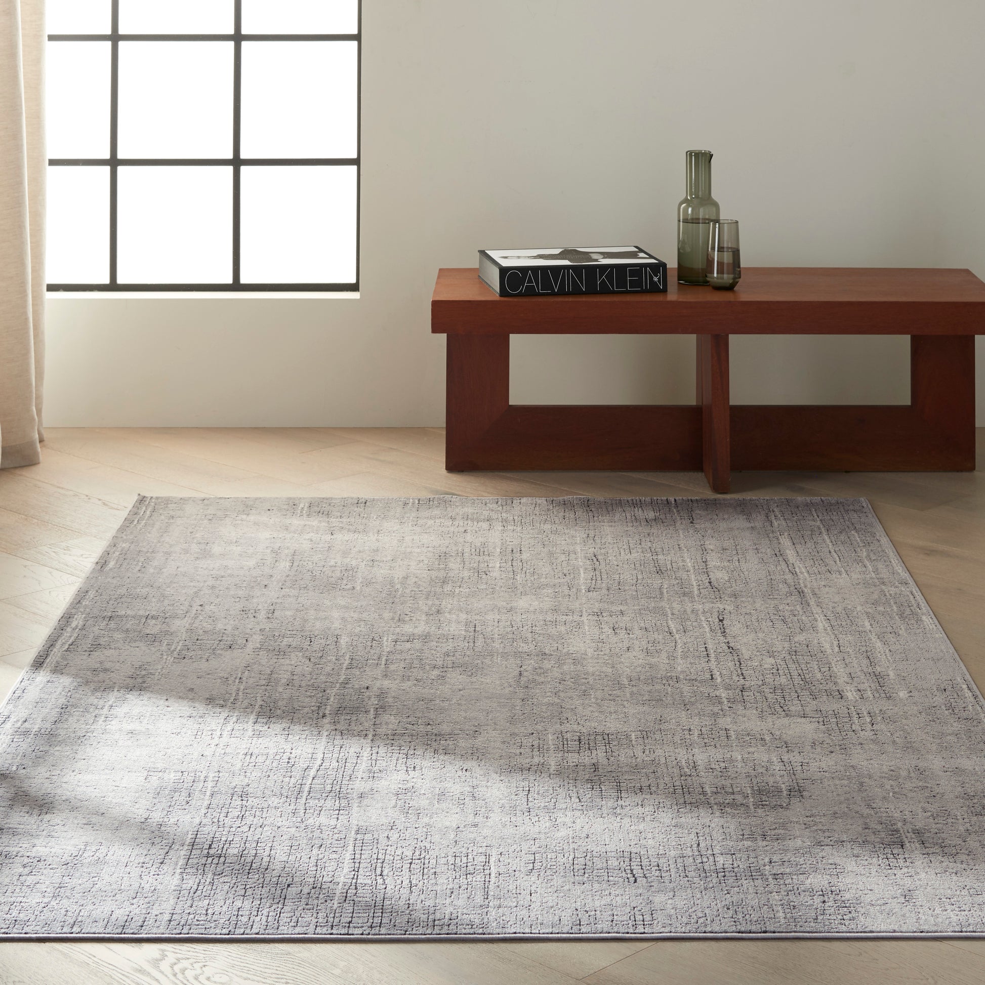 Minimalist living room: low rectangular wooden coffee table with a C K Design book and glassware, atop a grey textured rug.