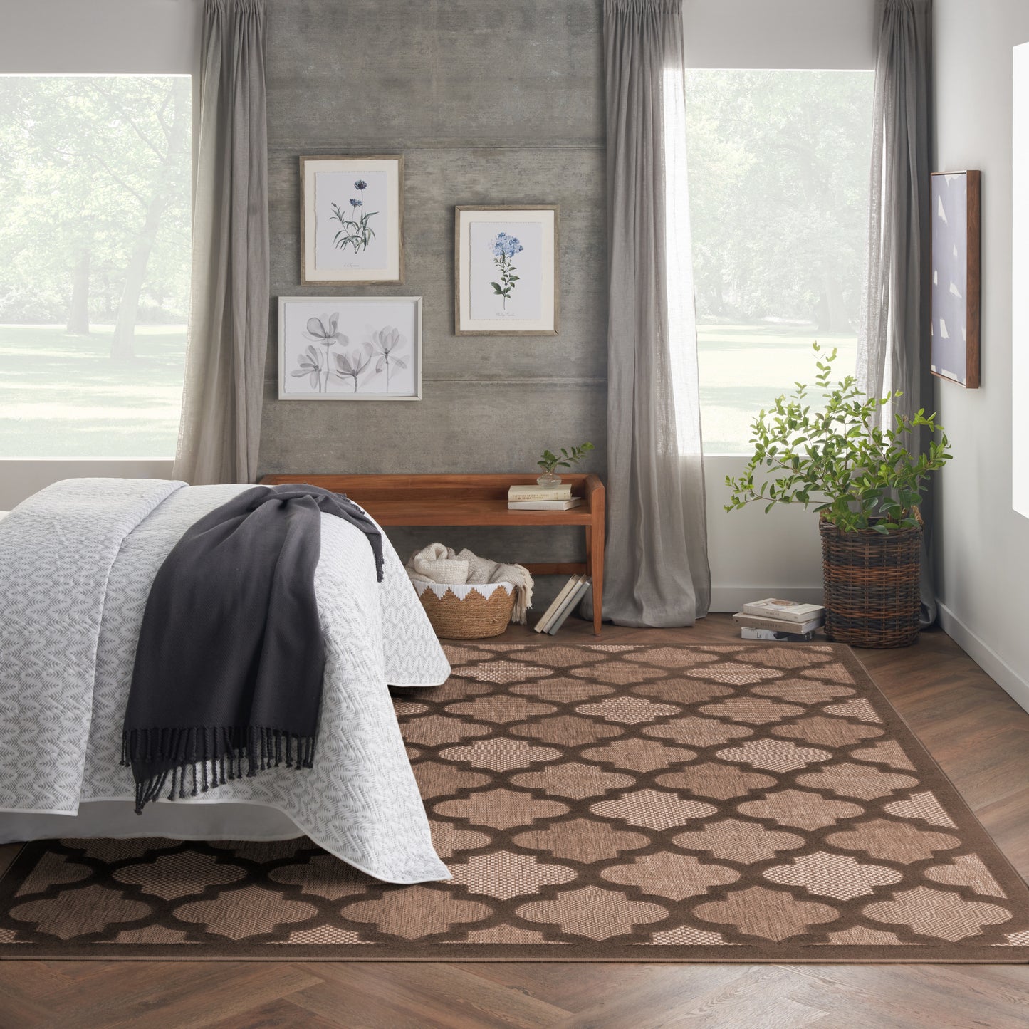 Cozy modern bedroom with white quilted bed, gray throw, brown rug, concrete wall, art, large windows, potted plant.