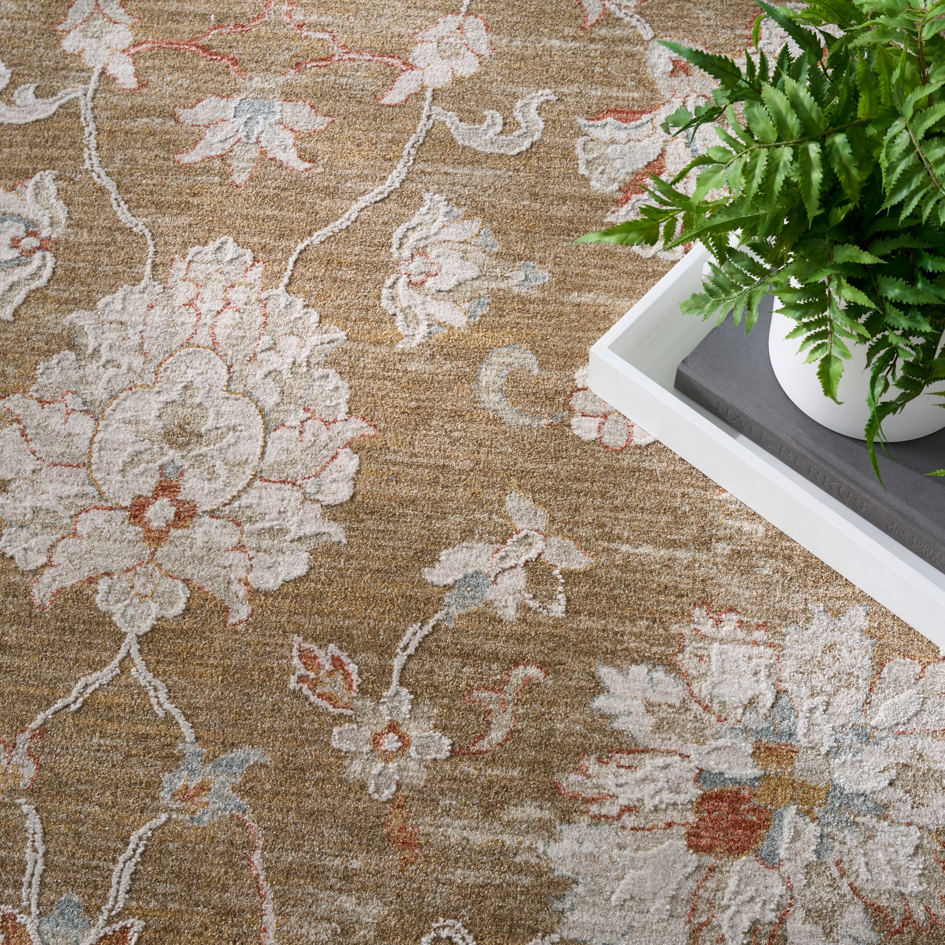 Beige floral area rug with cream, pink and blue accents; white tray with a potted fern for modern decor.