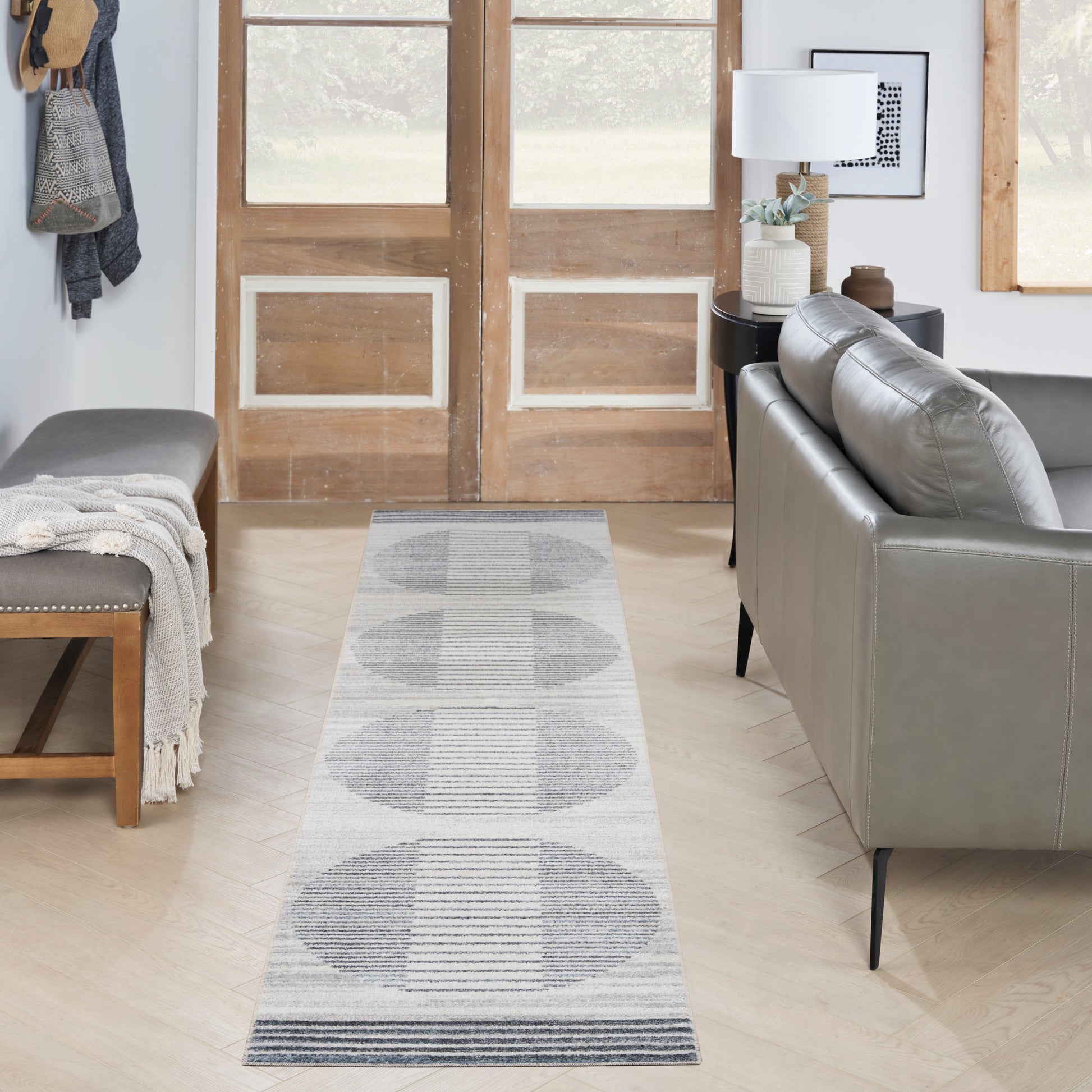 Gray & white geometric runner rug with circular patterns in a modern living room entryway; wood doors & a gray sofa.