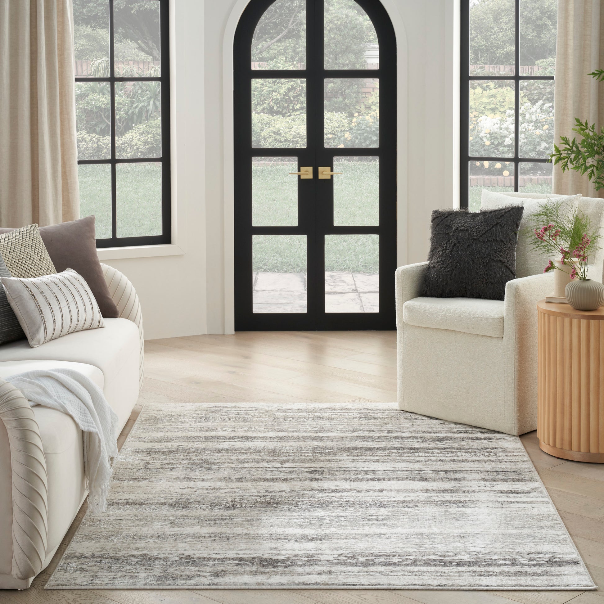 Cozy living room with an arched black door, beige sofas, striped gray rug, light wood floors, and a side table with plant.