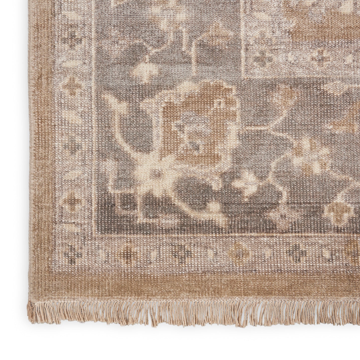 Corner view of a beige-taupe oriental rug with floral border and fringe trim.