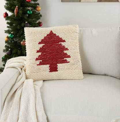 Beige knitted square cushion featuring a red Christmas tree; on cream sofa with a cream throw nearby.