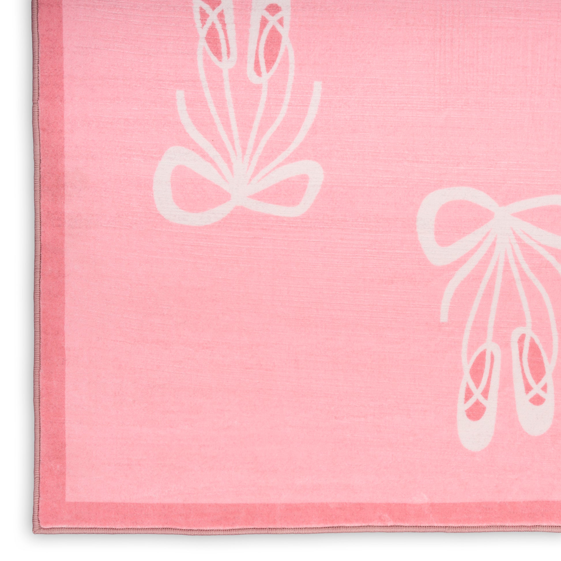 Pink rug with white ballet slipper bow motifs; plush pile and stitched edge.
