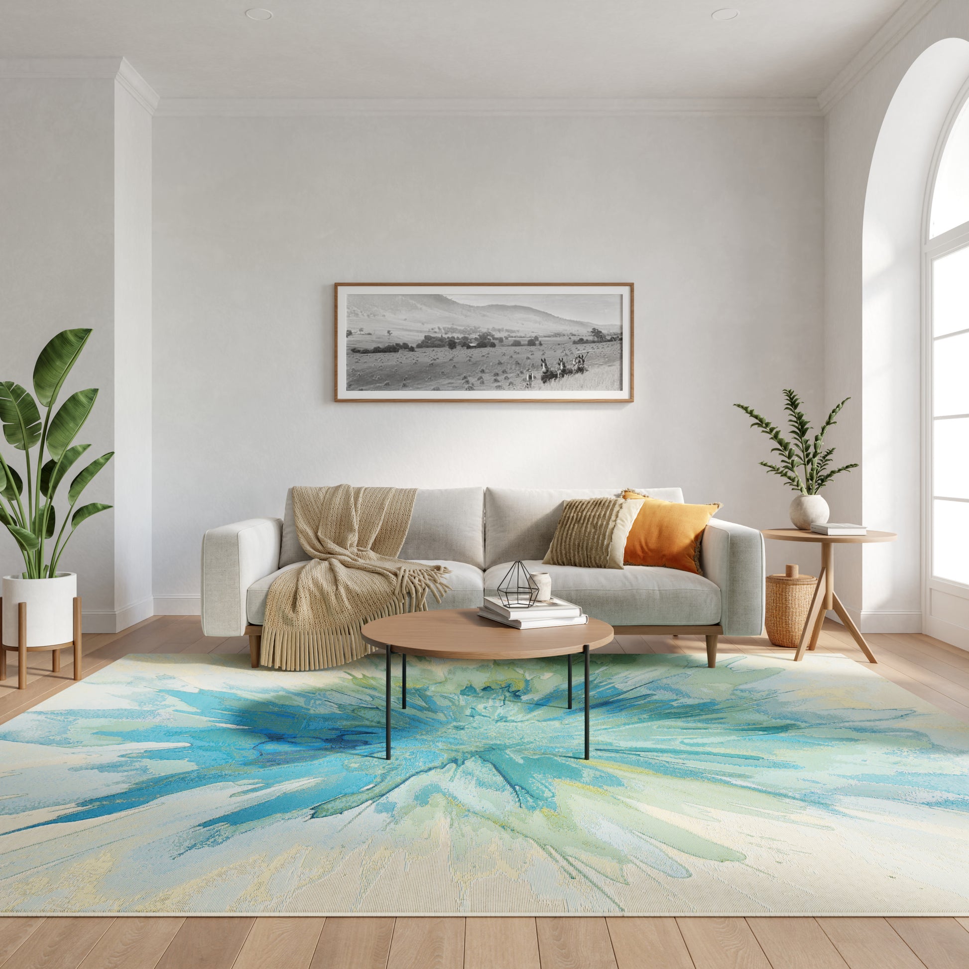 Modern living room: gray sofa, beige throw, orange cushion, round wood coffee table, blue-green abstract rug, plants.