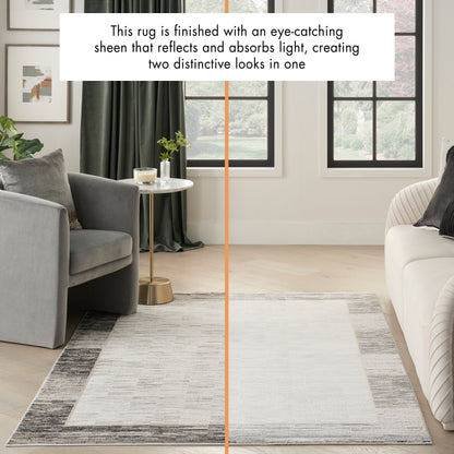Rectangular two-tone rug with light ivory center and charcoal-gray border; modern living room with gray chairs and sofa.