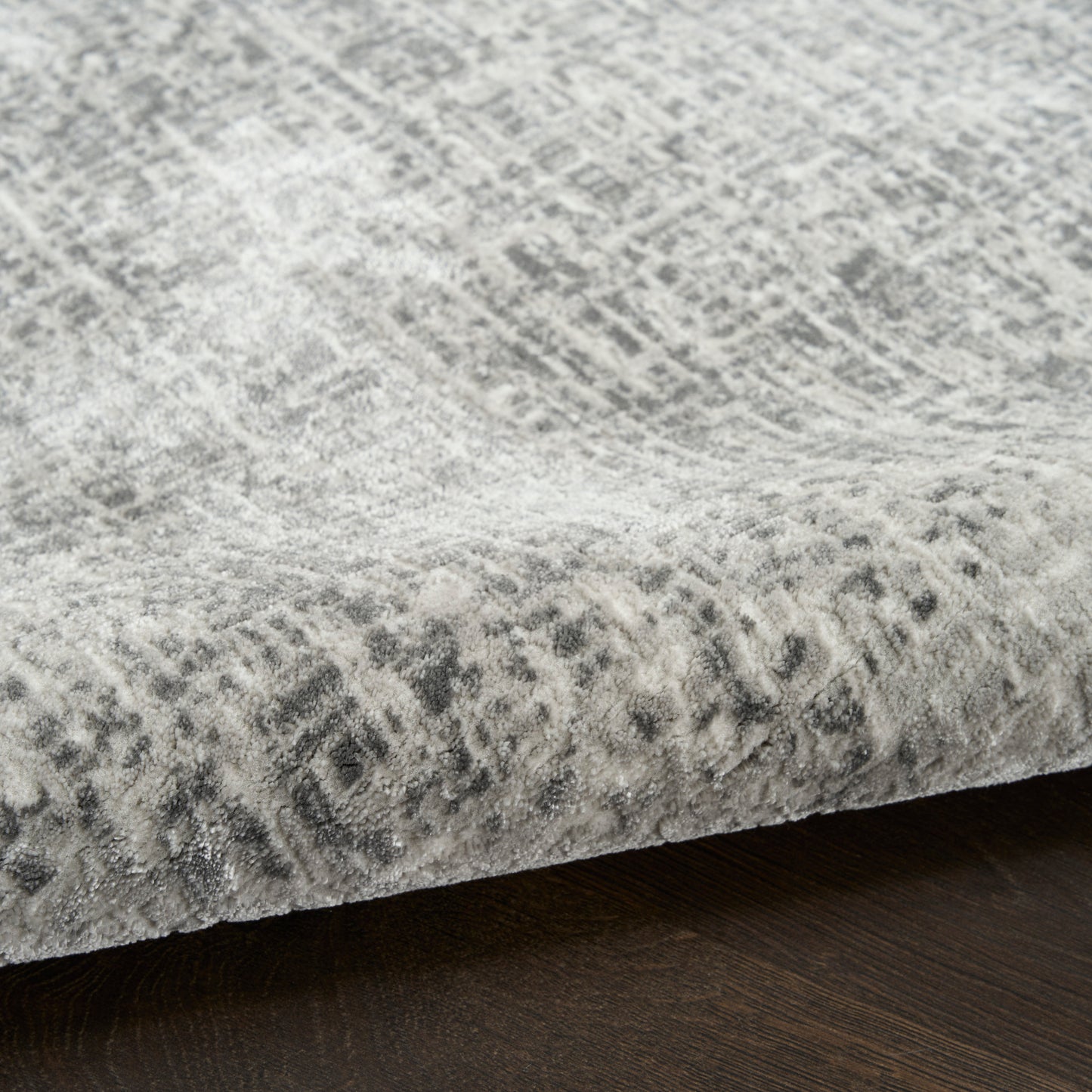 Grey abstract patterned rug with distressed geometric design on dark wood floor.
