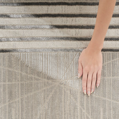 Beige textured rug with geometric line pattern and a hand with nude nails resting on it.