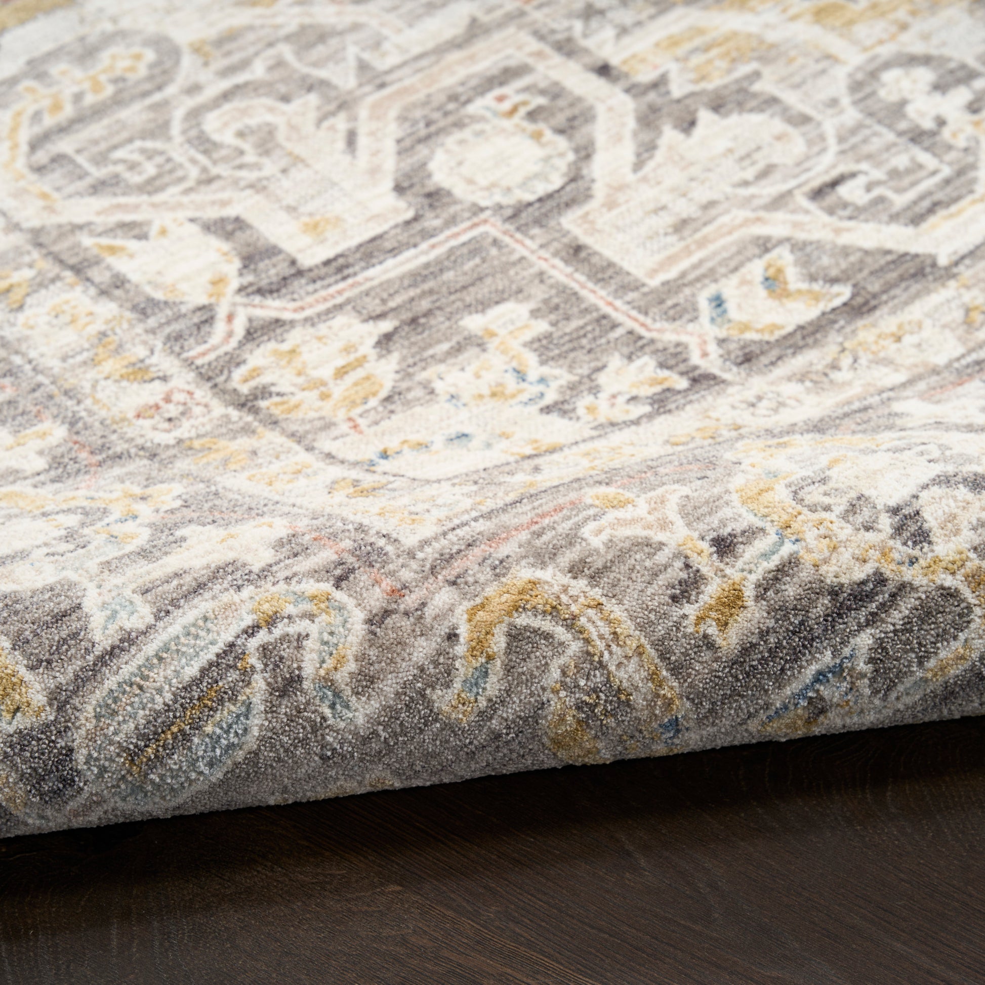 Close-up of an ornate patterned rug with ivory, gray, yellow and pale blue tones; woven texture and folded edge.