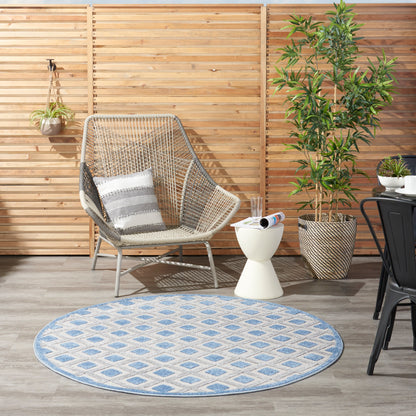 Round blue-and-white geometric outdoor rug under a woven rattan egg chair with striped cushion, beside potted plants and a white side table.