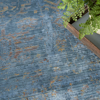 Blue abstract-pattern area rug with orange and gold accents, wooden plant stand and green fern in corner.