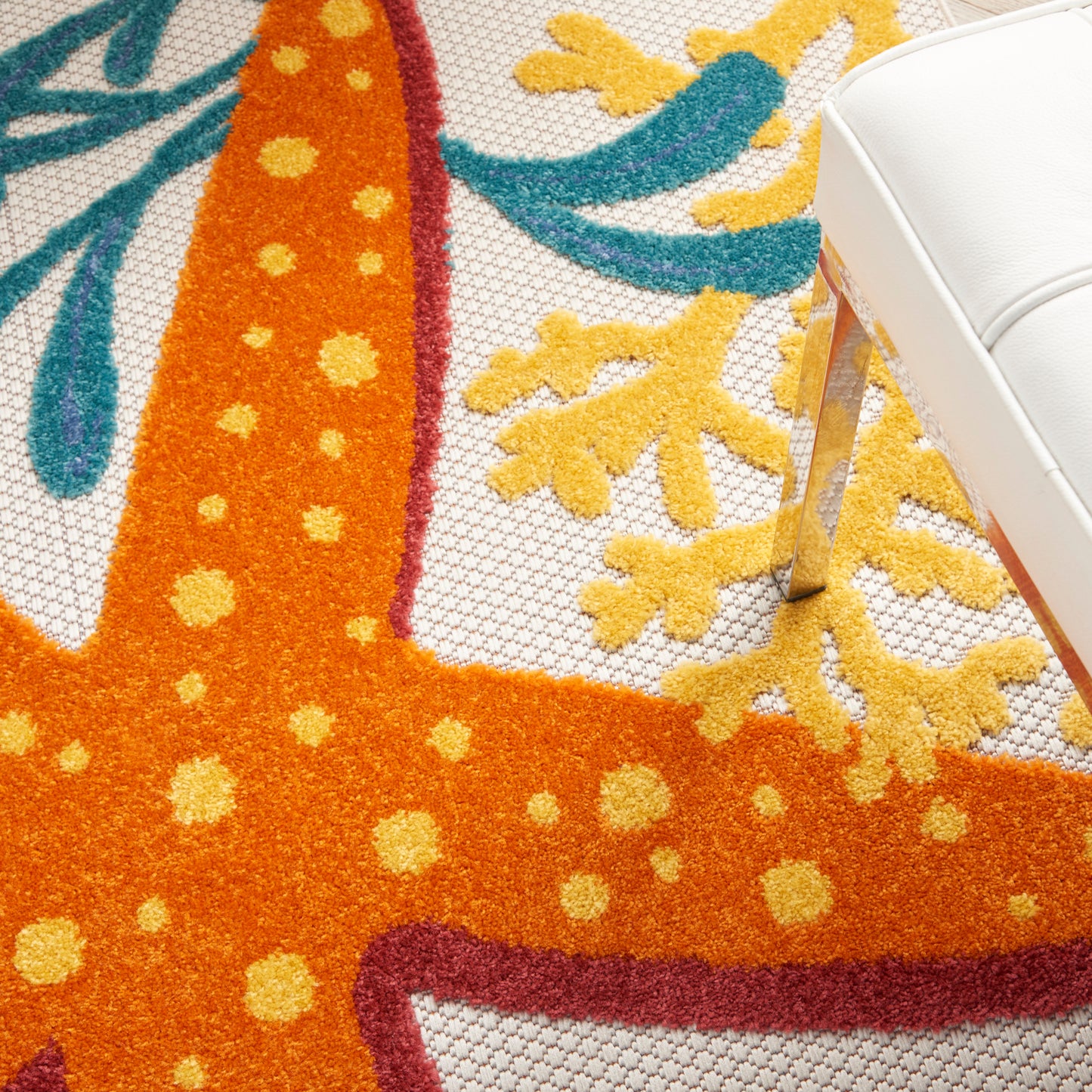 Bright orange shag rug with yellow polka dots and teal floral accents; modern tropical design beside a white chair.