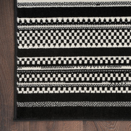 Rectangular black and white flatwoven rug with checkerboard and stripe patterns, bordered in black on a wooden floor.