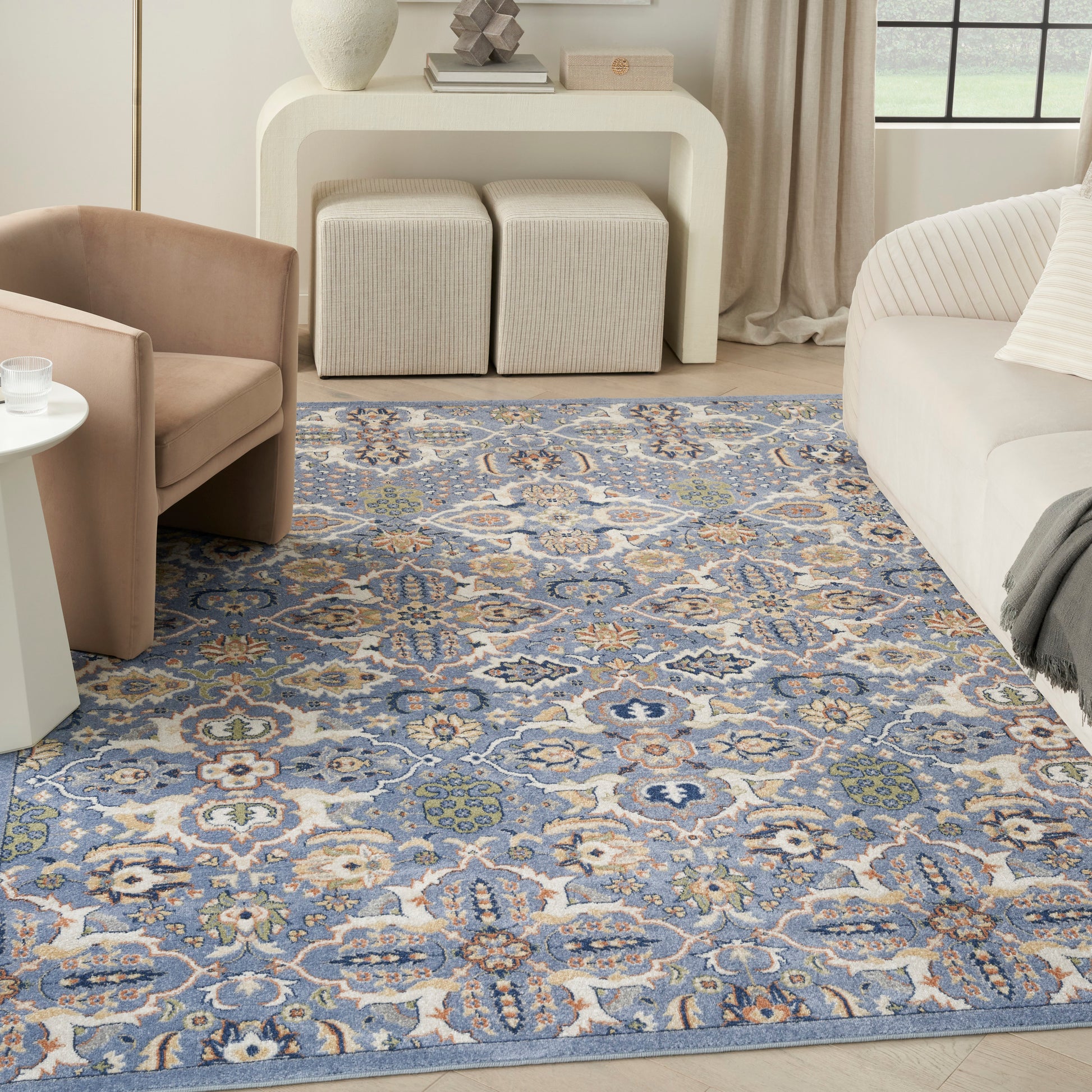 Blue floral area rug in a light living room with a cream sofa, blush armchair, white console, and square ottomans.